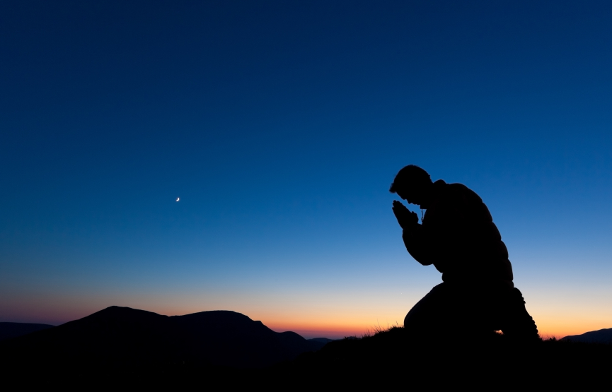 Man praying on the summit of a mountain at sun set with the moon in the sky.